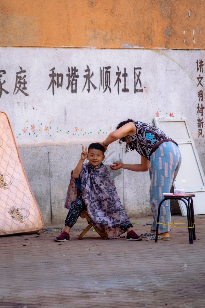 Paint By Numbers | Dalian - Boy Sitting On Stool Beside Standing Woman Near Wall - Custom Paint By Numbers