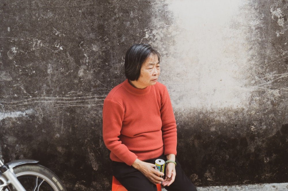 Paint By Numbers | Jieyang - Woman In Orange Sweater Standing Beside Gray Concrete Wall - Custom Paint By Numbers