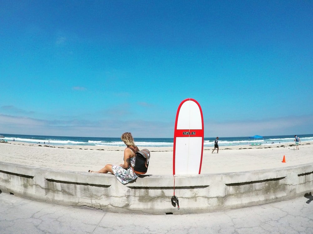 Paint By Numbers | San Diego - Woman Sitting On White Concrete Barrier Beside Skimboard During Daytime - Custom Paint By Numbers